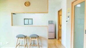 A small kitchenette with a microwave, a refrigerator, and two bar stools. - Heartwarming House (Kyoto)