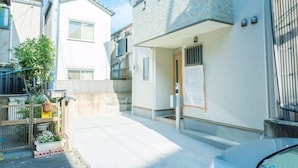 A residential building with a white exterior, a visible entrance, and a small garden area with potted plants. - Heartwarming House (Kyoto)