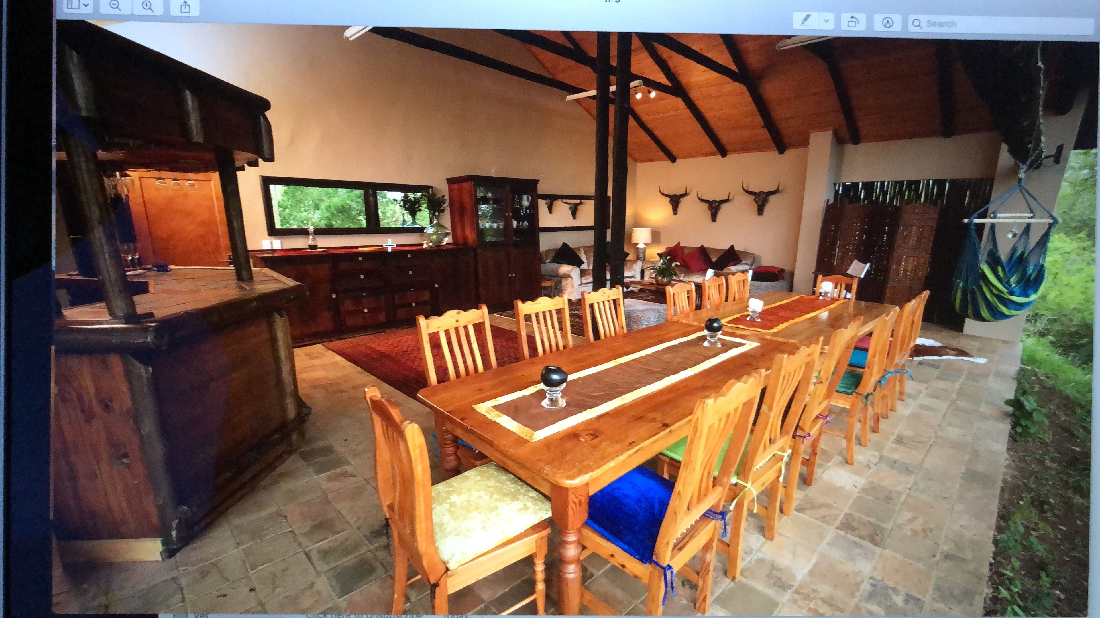A spacious dining area with a long wooden table and chairs, a bar area with a wooden counter, and a view of the outdoors through a large window.