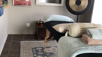 Cozy retreat with a bed, bedside table, and wall-mounted shelf, featuring a large mirror and a decorative gong.