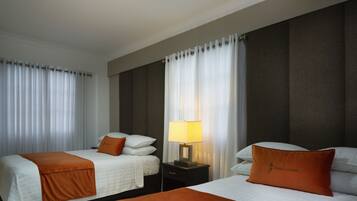 Una habitación de hotel con dos camas, una mesita de noche con lámpara y un ventanal con cortinas.
