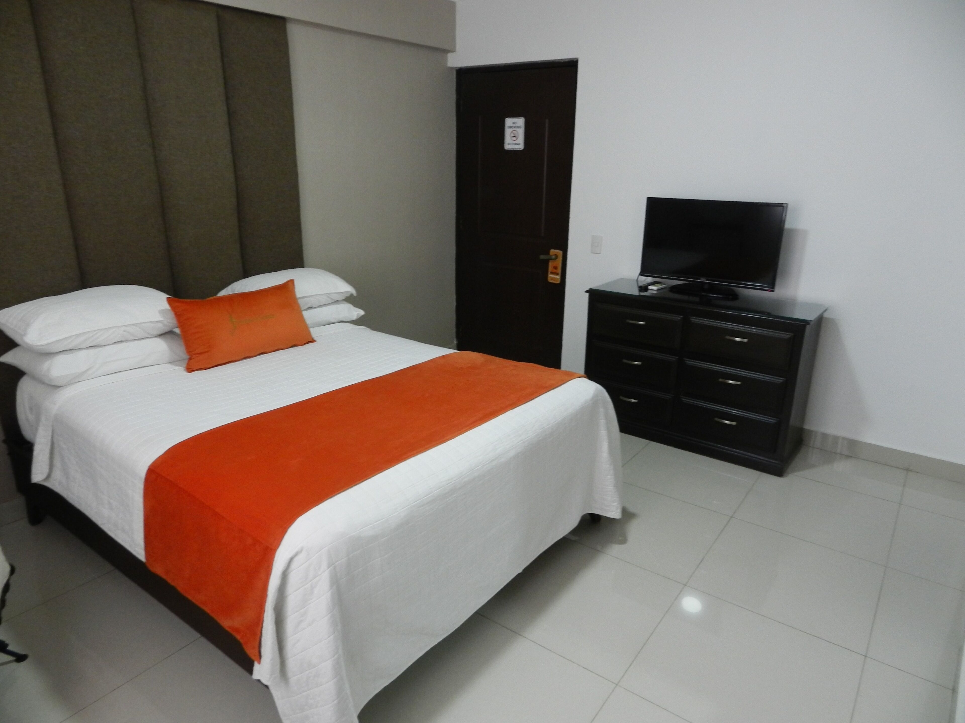 A hotel room with a bed, a television on a dresser, and a door with a sign.