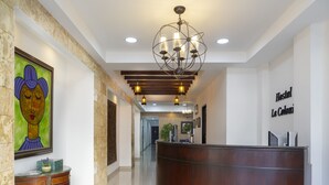 A hotel reception area with a wooden reception desk, a chandelier, and a framed artwork on the wall.