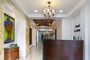 A hotel reception area with a wooden reception desk, a chandelier, and a framed artwork on the wall.