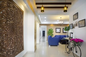 A modern living room with a blue sofa, a bicycle with a flower basket, and a decorative wall panel.