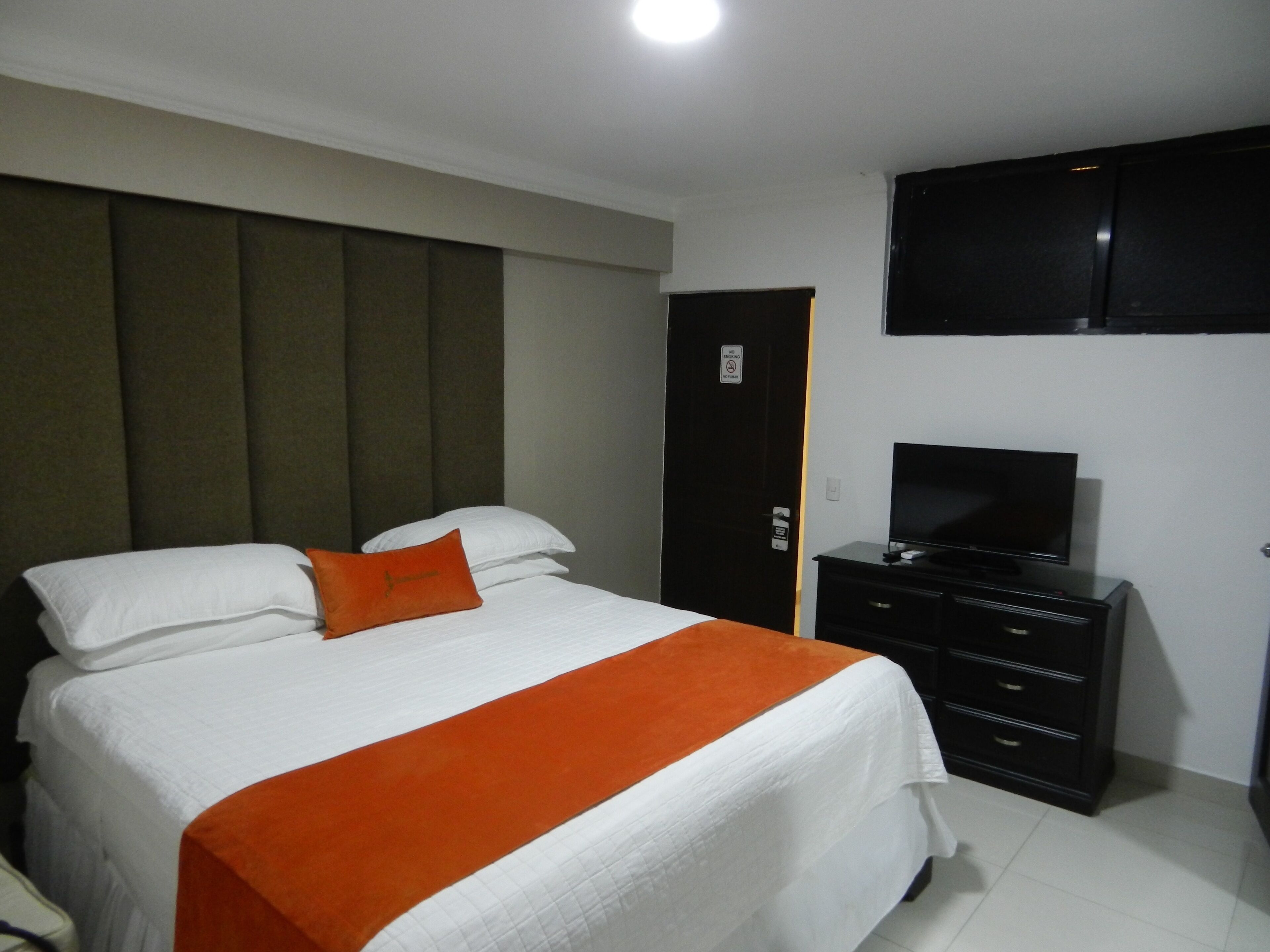 A hotel room with a bed, a TV, a wardrobe, and a door with a sign.