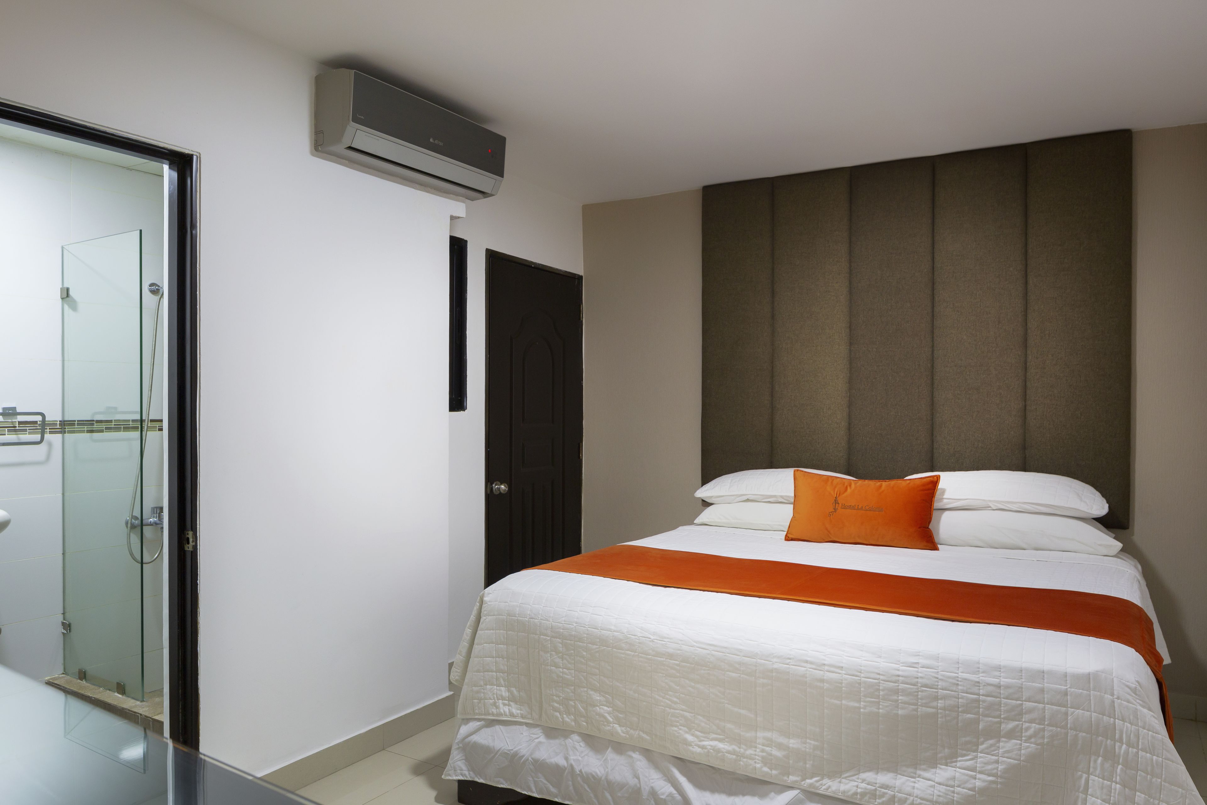 Een hotelkamer met een bed, een glazen douchecabine en een wandairconditioner.