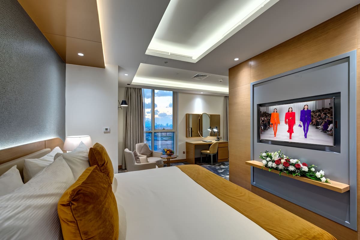 Ein Hotelzimmer mit einem großen Bett, einem Schreibtisch, einem Sessel, einem Fernseher und Blick auf die Stadt.