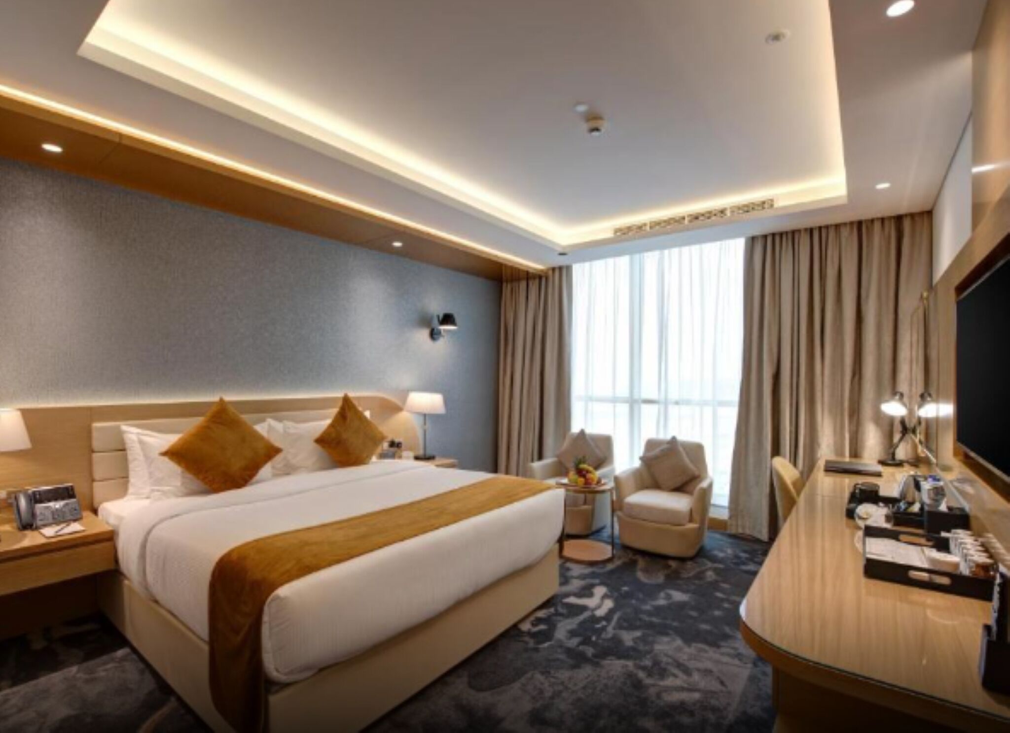 A hotel room with a large bed, a desk, a chair, and a TV.