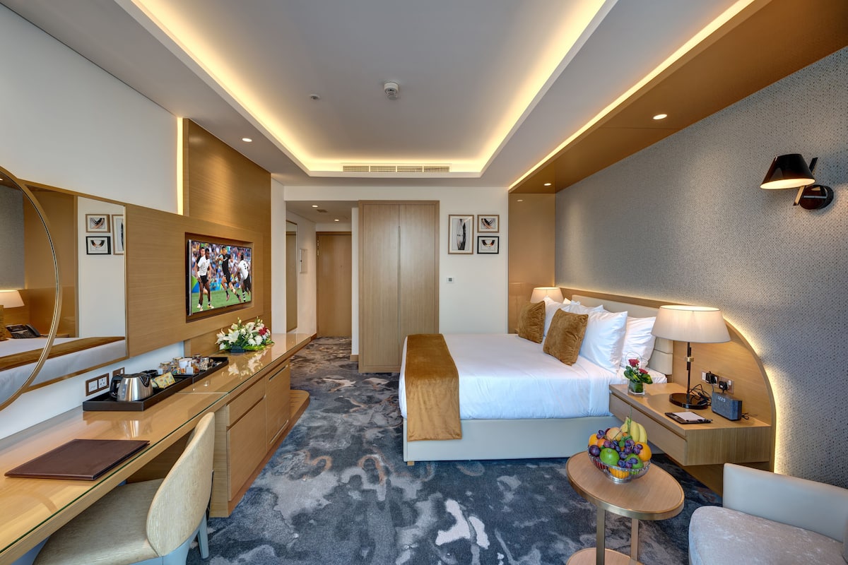 Ein Hotelzimmer mit Bett, Schreibtisch, Stuhl, Nachttisch und einem an der Wand befestigten Fernseher.