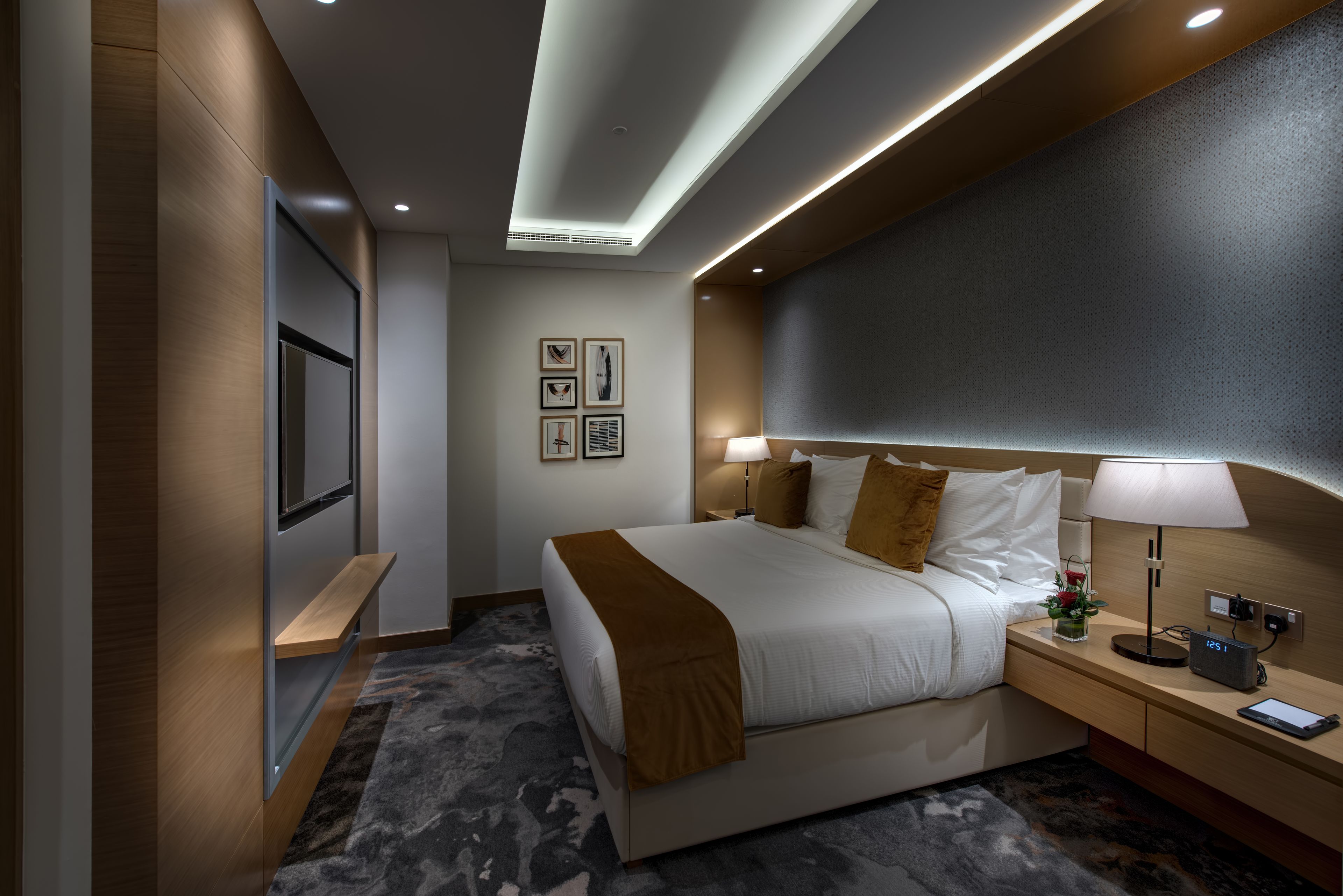 A modern hotel room with a large bed, bedside tables, a flat-screen TV, and a desk lamp.