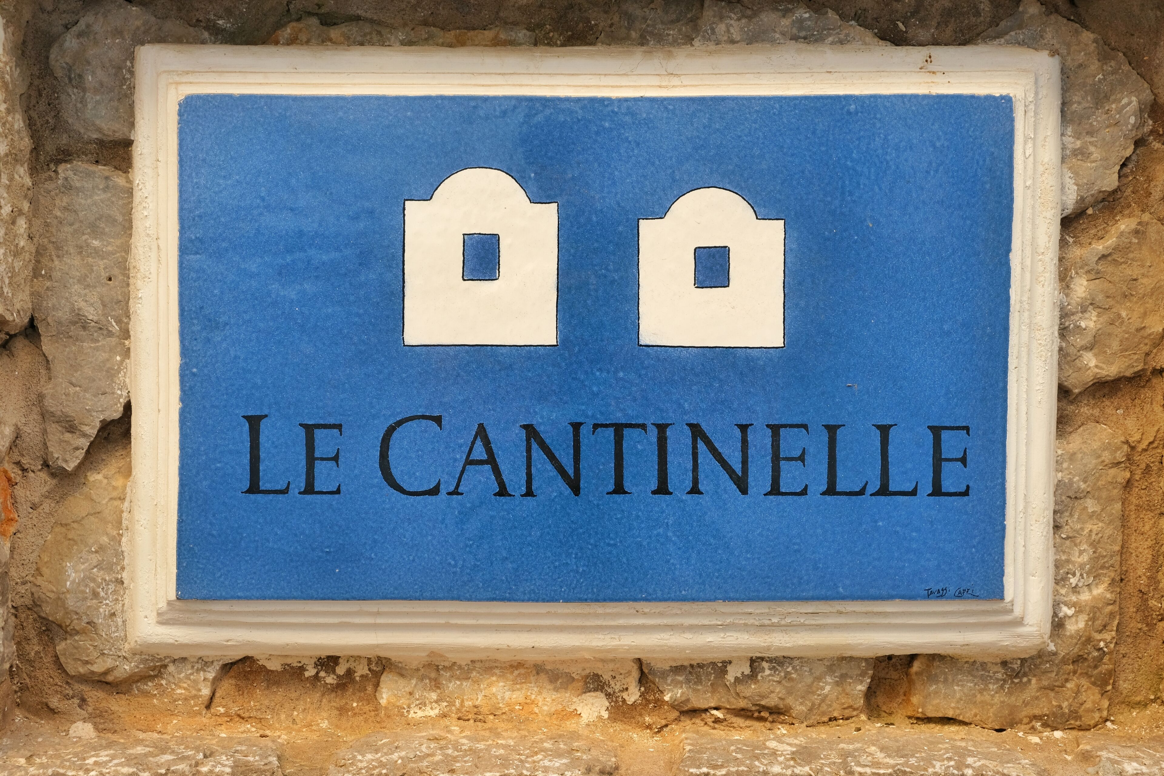 A blue sign with white text and symbols, mounted on a stone wall.