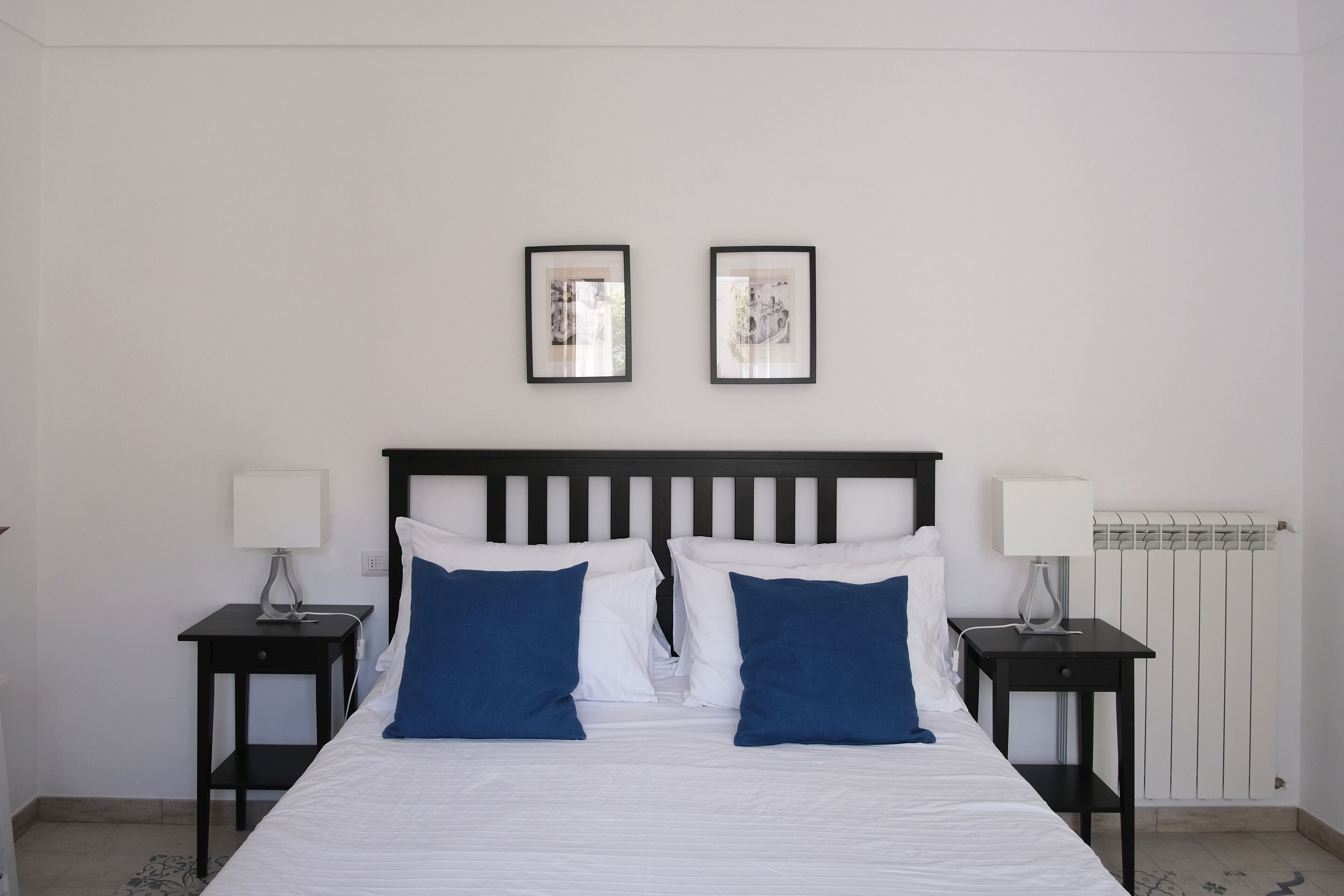A neatly made bed with white and blue pillows, two bedside tables with lamps, and two framed pictures on the wall.