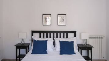 A neatly made bed with white and blue pillows, two bedside tables with lamps, and two framed pictures on the wall.