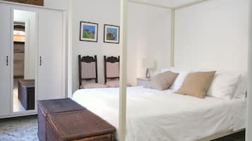 A bedroom with a four-poster bed, a wicker chest of drawers, and a nightstand with a lamp.