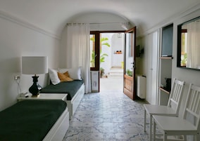 Ein Schlafzimmer mit Bett, Nachttisch, Lampe und einem Sessel. Eine Tür führt auf einen Balkon mit Pflanzen.