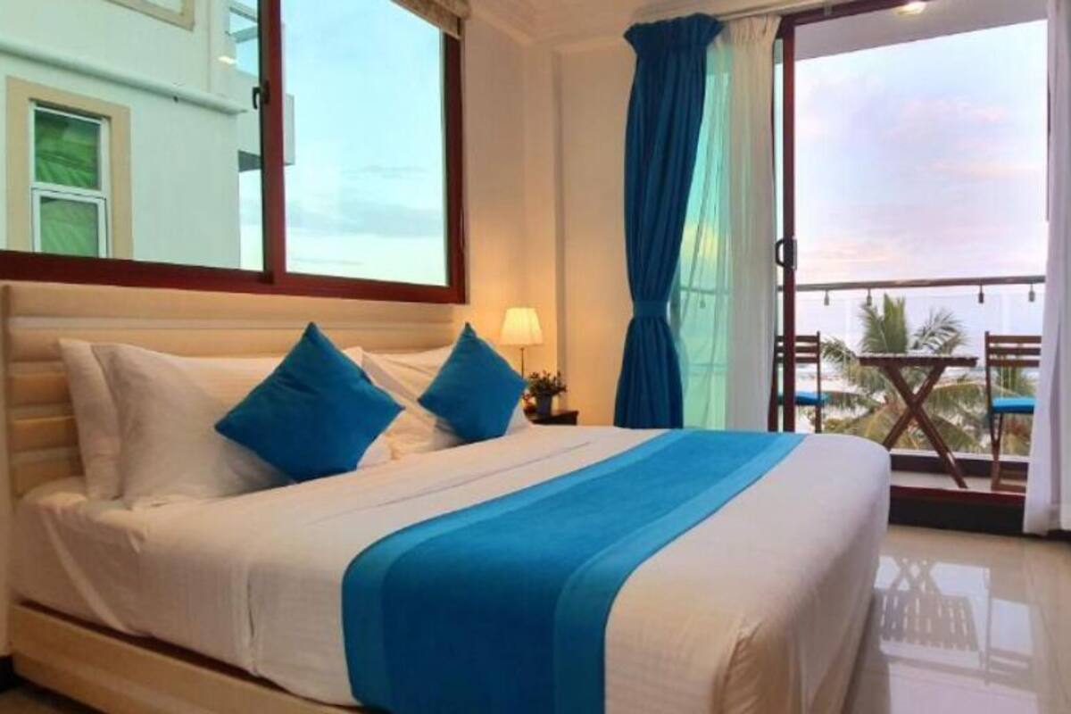 Een hotelkamer met een bed, nachtkastje, dressoir en een balkon met uitzicht.
