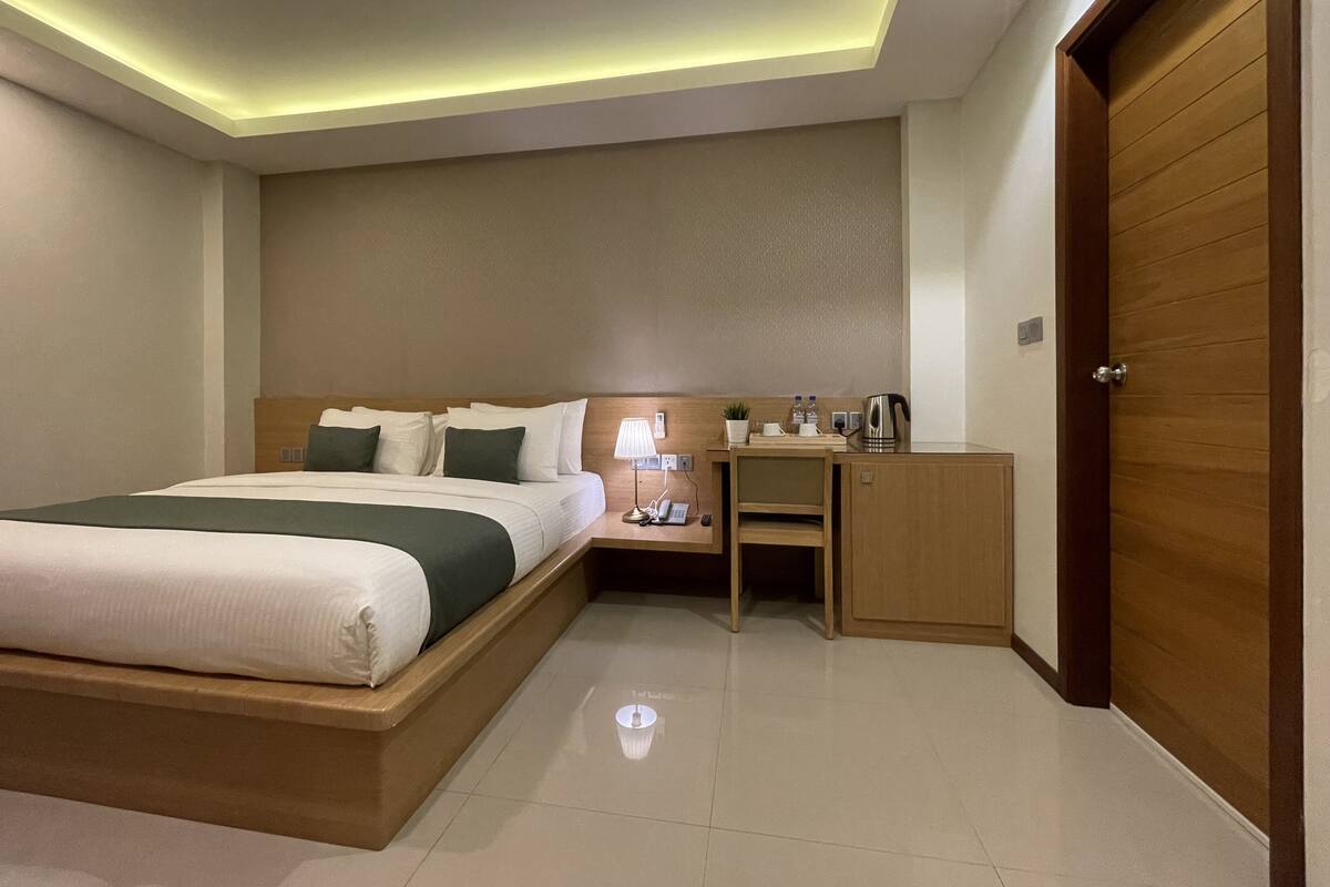 Een hotelkamer met een bed, nachtkastje, lamp en een houten deur.