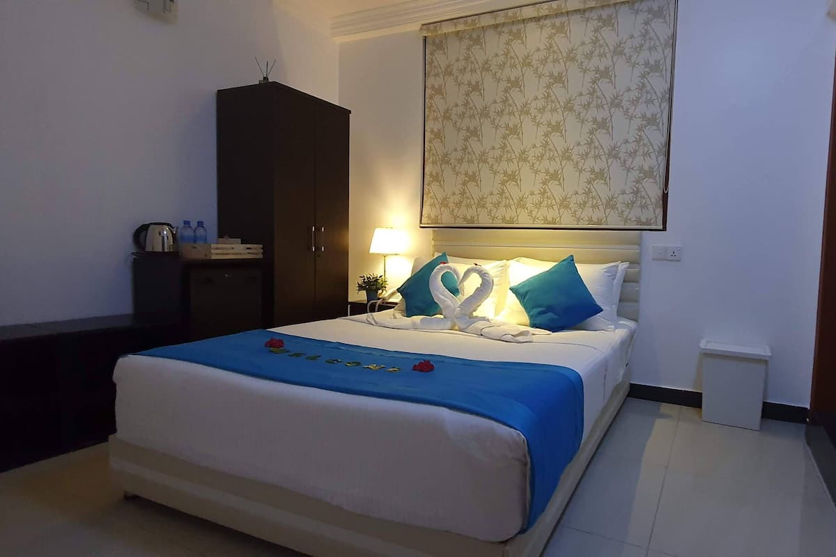 Een netjes ingerichte hotelkamer met een bed, een kledingkast, een nachtkastje met een lamp en een kleine prullenbak.