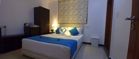 Habitación de hotel ordenada con cama, armario, mesita de noche con lámpara y un pequeño cubo de basura.