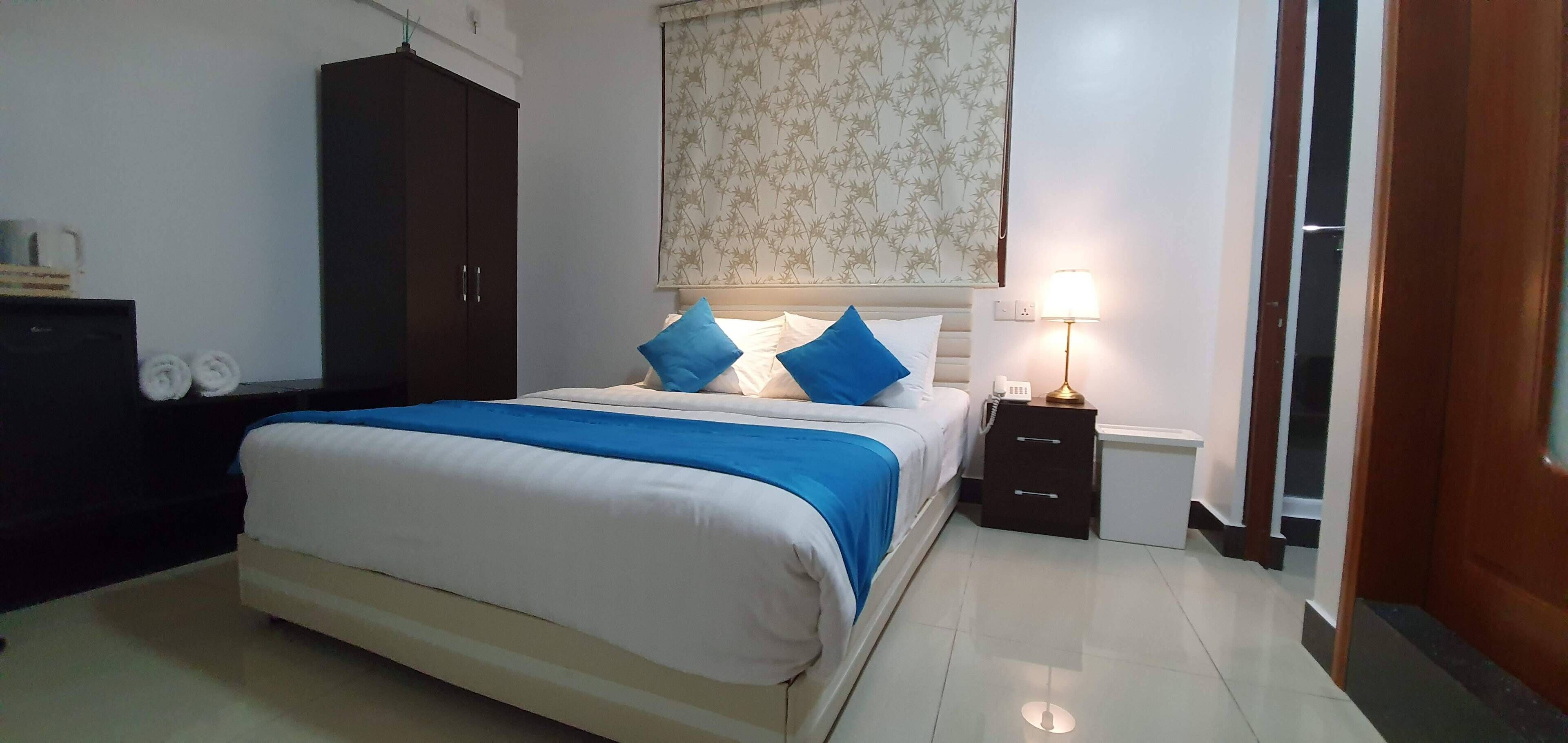 Un dormitorio ordenado con una cama, un armario, una mesita de noche con lámpara y una pared con estampado floral.