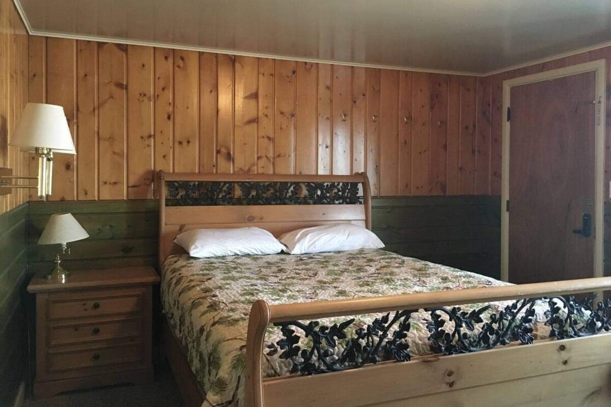 A wooden-paneled bedroom with a bed, a nightstand, and a lamp.