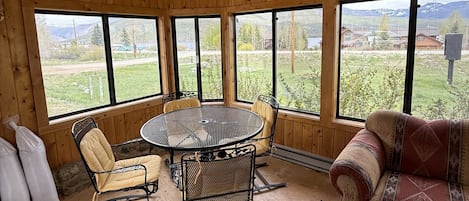 Un intérieur en bois avec une table ronde, deux chaises, un canapé et de grandes fenêtres donnant sur un paysage verdoyant.