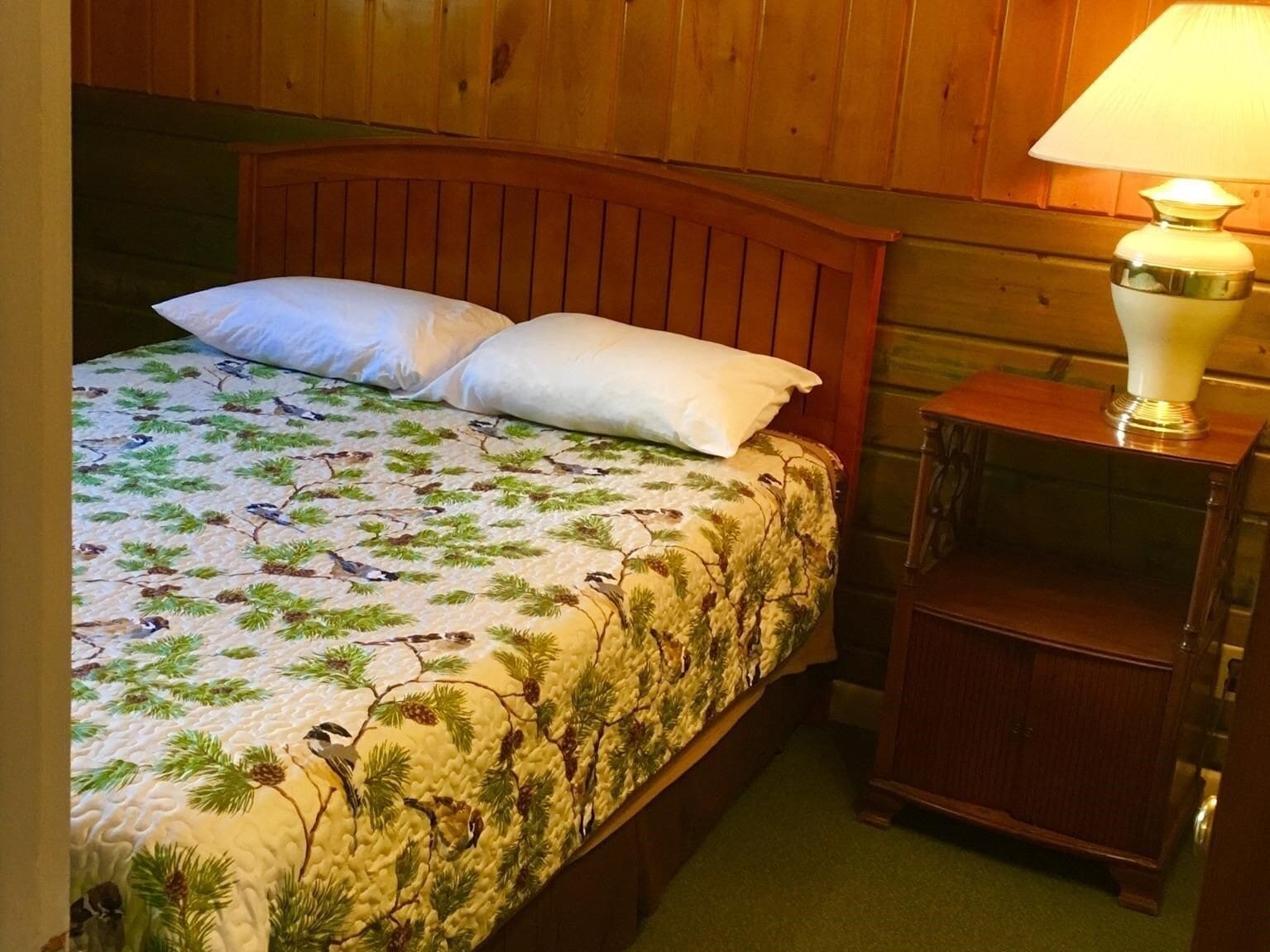 A bed with a floral bedspread, two pillows, and a wooden headboard.