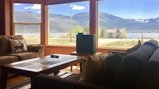A living room with a large window, a television on a stand, and a table with a placemat. - Timberline Inn of Grand Lake (Grand Lake)