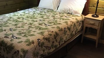 Una cama con una colcha estampada, dos almohadas, una mesita de noche con una lámpara y un cabecero de madera.