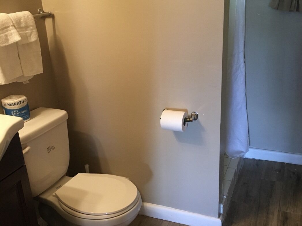 Un baño con inodoro, un rollo de papel higiénico y un rollo de toallas de papel sobre el mostrador.