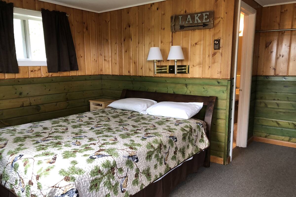 A bedroom with a bed, two bedside lamps, a wooden headboard, a window with curtains, and a sign that says "LAKE".