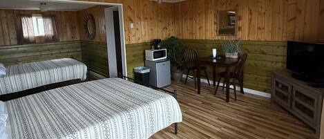 Une chambre avec deux lits, une petite table avec des chaises, un téléviseur et un ventilateur de plafond.