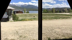 A view through a window of a building with a gravel yard, a wooden cabin, and a lake with mountains in the background. - Timberline Inn of Grand Lake (Grand Lake)