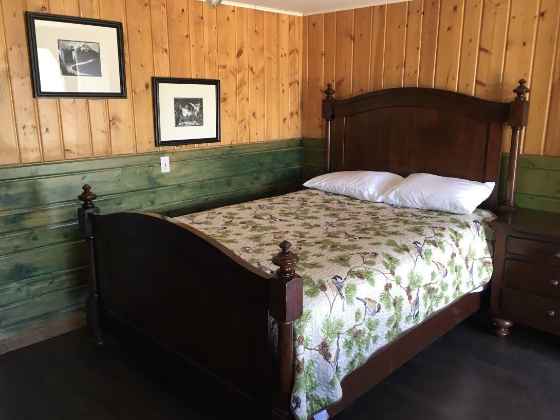 A wooden-paneled room with a bed, framed pictures on the wall, and a dresser.