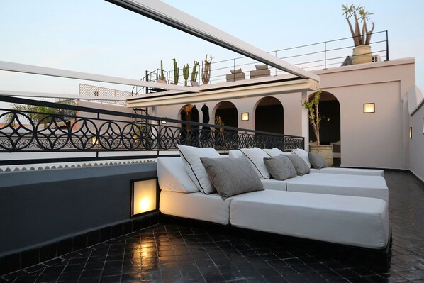 A modern outdoor seating area with a white sofa and cushions, a decorative metal railing, and potted plants. - Riad Dar Bahi (Marrakech)