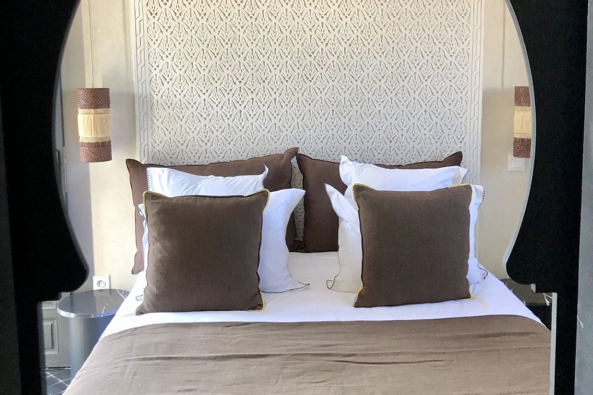 A bed with a patterned headboard, brown and white pillows, and a beige bedspread.