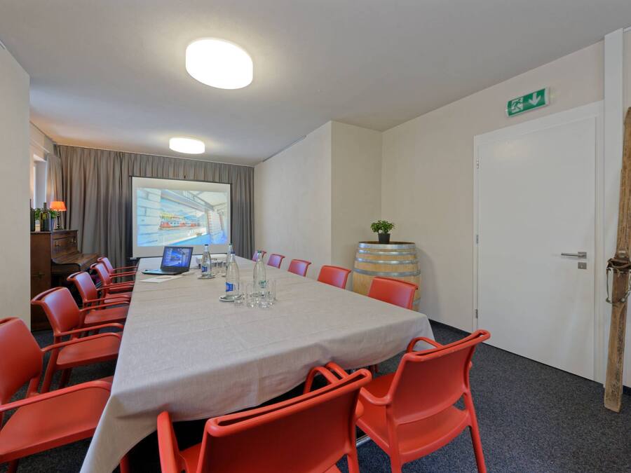A conference room with a long table, red chairs, a projector screen, and a wooden barrel.