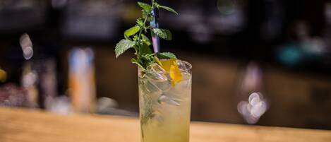 A clear glass of a yellowish beverage with mint leaves and an orange peel garnish on a wooden surface.