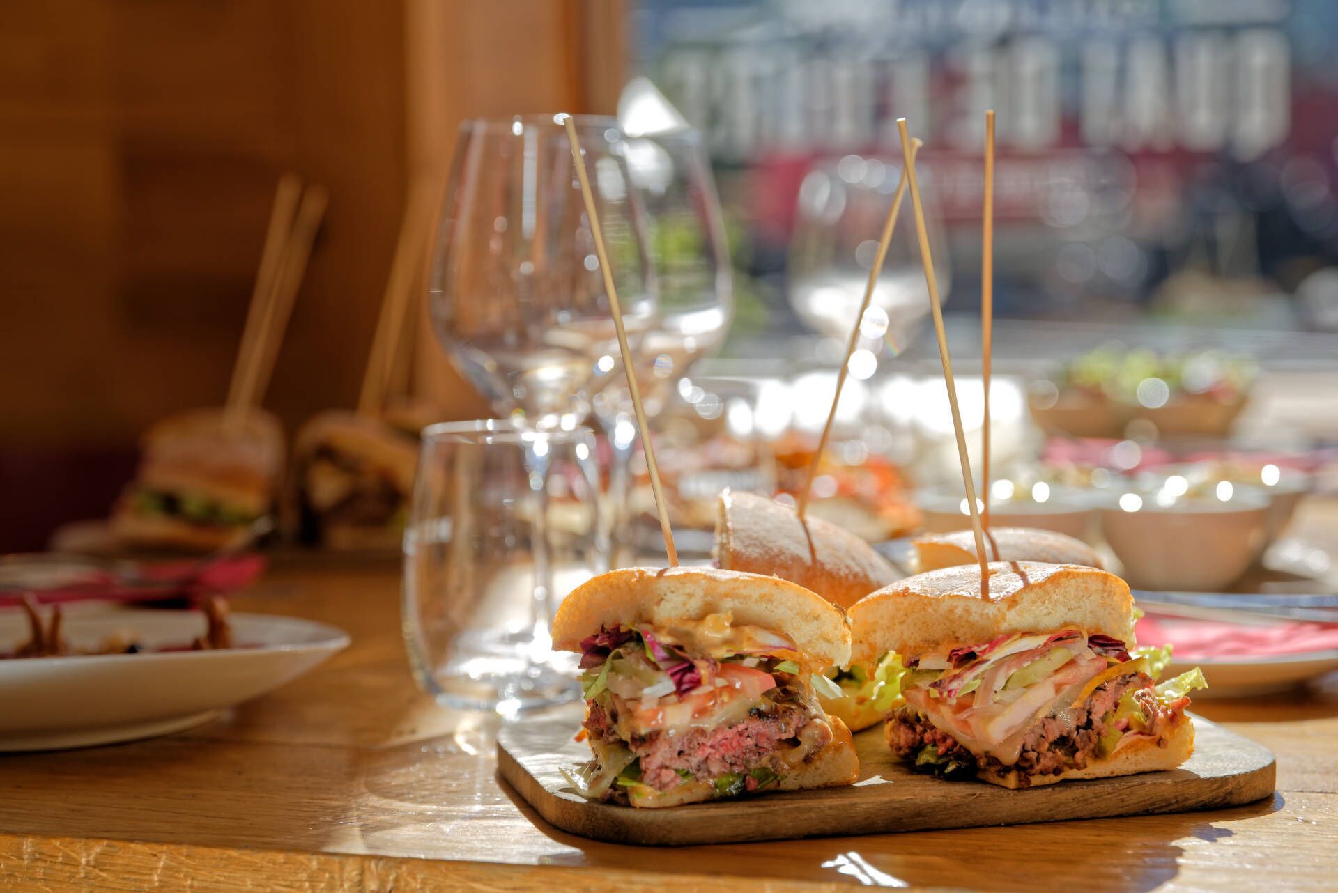 Een restaurantscène met belegde broodjes op houten planken, glazen en een vage achtergrond van andere gerechten.