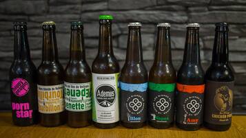 Varias botellas de cerveza con diferentes etiquetas y diseños, dispuestas sobre una superficie de madera frente a un fondo de pared de piedra.