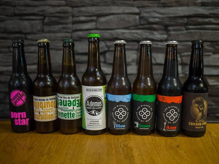 Varias botellas de cerveza con diferentes etiquetas y diseños, dispuestas sobre una superficie de madera frente a un fondo de pared de piedra.