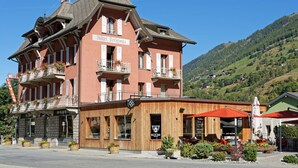 A hotel with a red facade, balconies with flower boxes, and a view of a green hillside. - Hôtel Terminus (Orsieres)