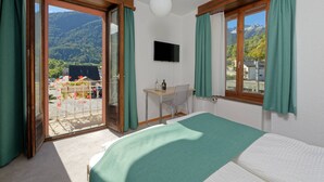 A bedroom with a bed, a desk, and a TV. It has a balcony with a view of the mountains. - Hôtel Terminus (Orsieres)