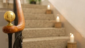 A staircase with a wooden handrail and brass finial, stone steps, and candles. - Hôtel Terminus (Orsieres)