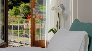 A bedroom with a bed, a window with a view of greenery and a red flower, and a green pillow. - Hôtel Terminus (Orsieres)
