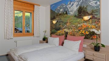 A bedroom with a bed, a window with curtains, a nightstand with a lamp, a wall-mounted shelf, and a painting of a mountain landscape.