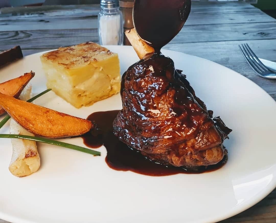 A plate with a glazed meat dish, a side of mashed potatoes, and roasted potatoes.