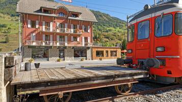 Un tren rojo en una estación, con un edificio que dice "HOTEL TERMINUS" al fondo.