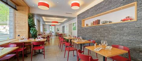 Ein modernes Restaurant mit roten Stühlen und Holztischen, einer Steinsäule mit Ablagefläche und großen Fenstern.